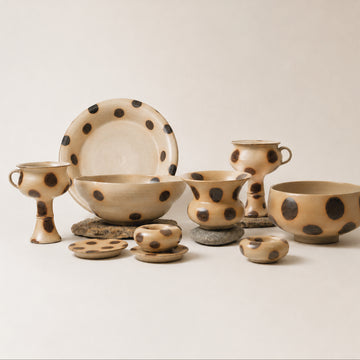 Set of ceramic bowls and cups with black polka dot patterns on a light background