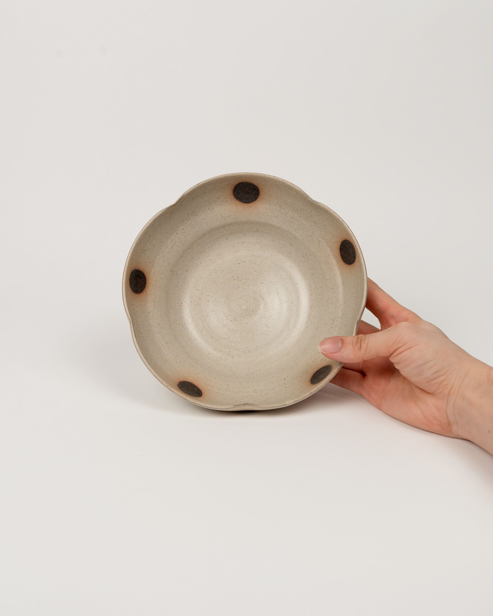 Hand holding a ceramic bowl with brown spots on a light gray background