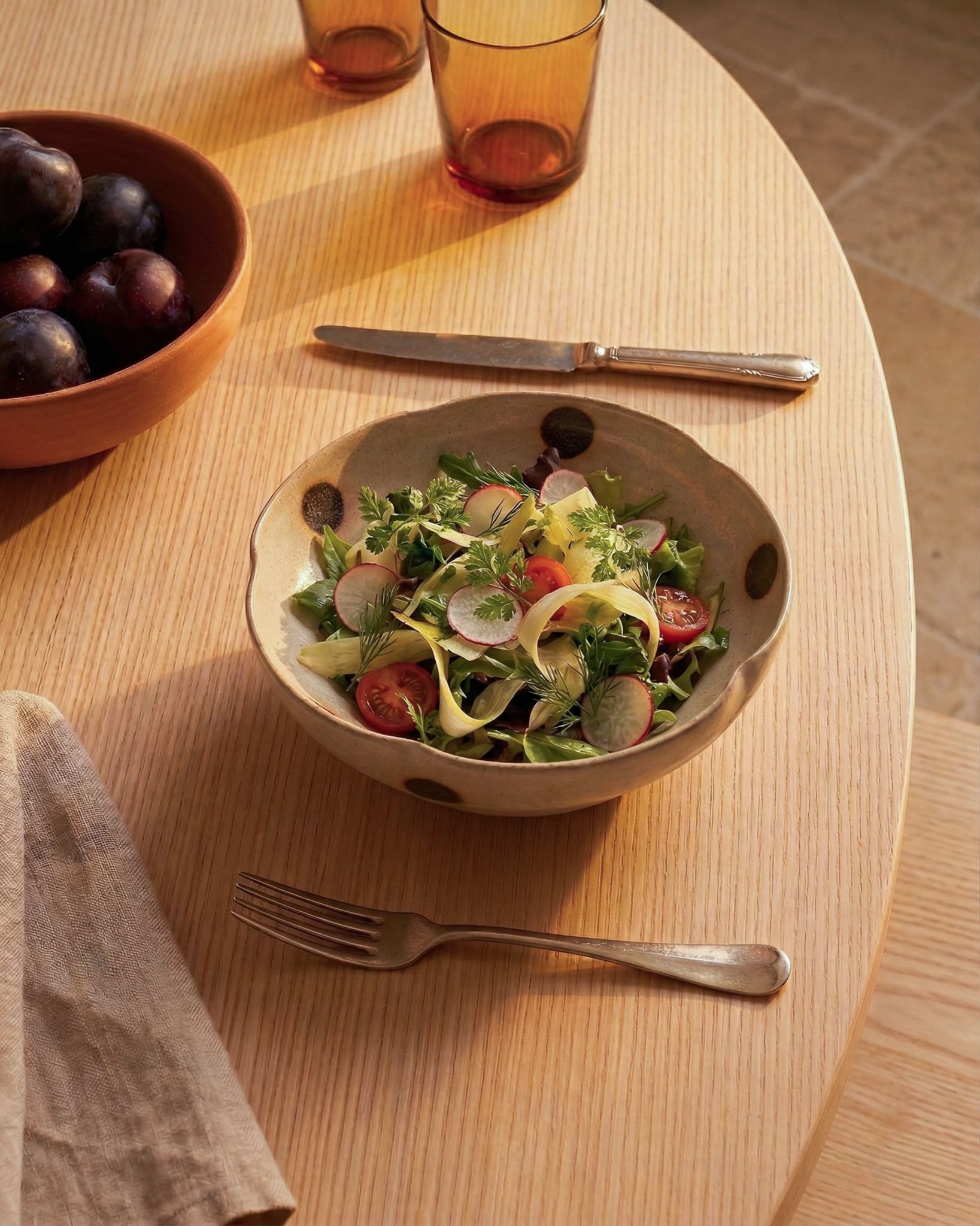 Bowl of salad on a wooden table with a fork and knife