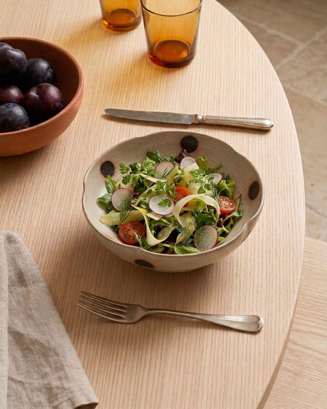 Bowl of salad on a wooden table with a fork and glasses in the background