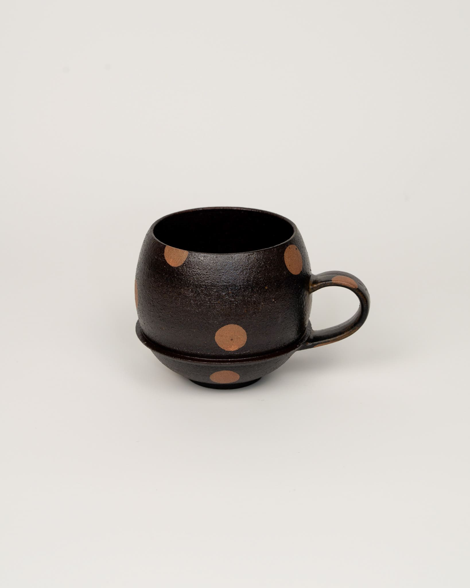 Black ceramic cup with brown polka dots on a light gray background