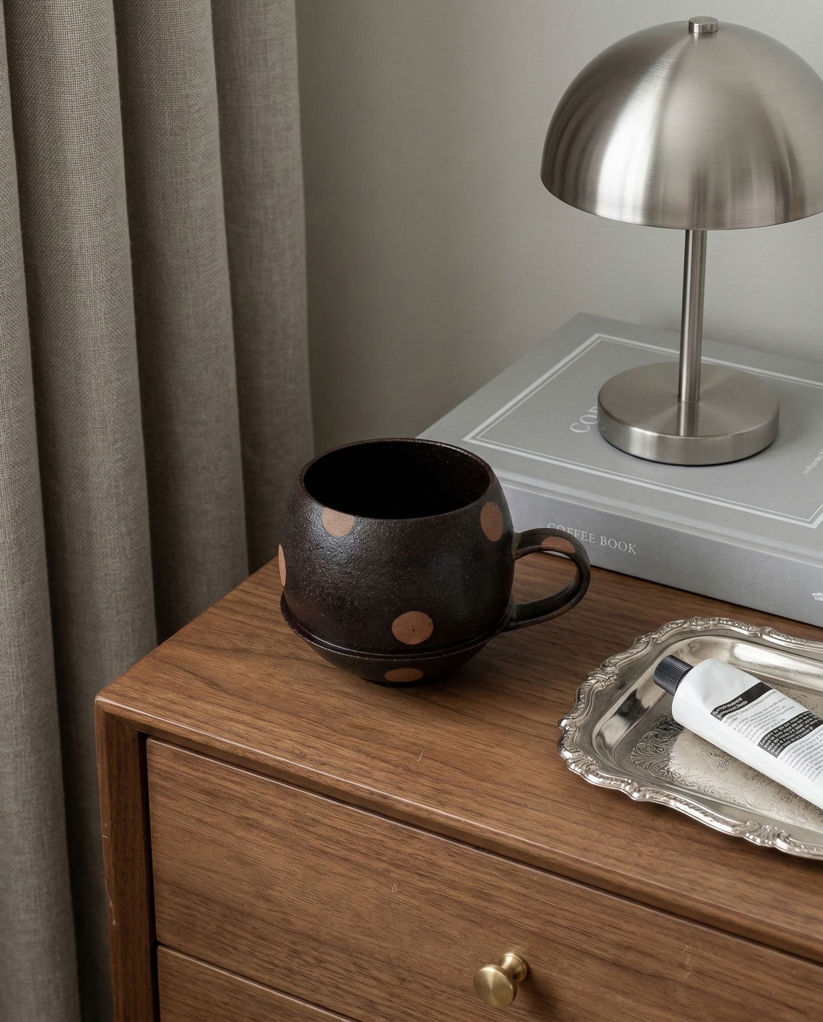 Black mug on a wooden dresser with a lamp and tray in the background