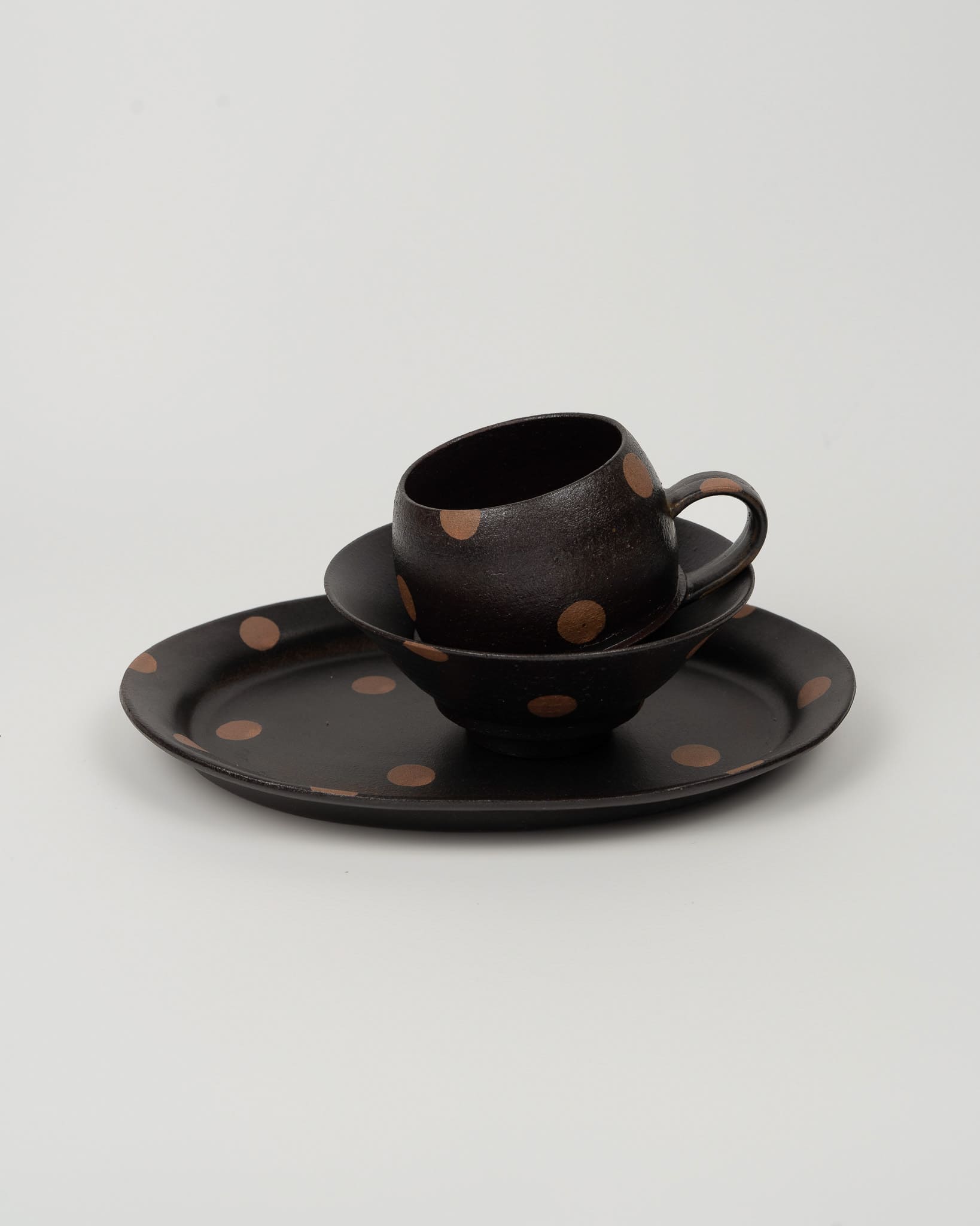 Black ceramic cup and saucer with brown polka dots on a light gray background