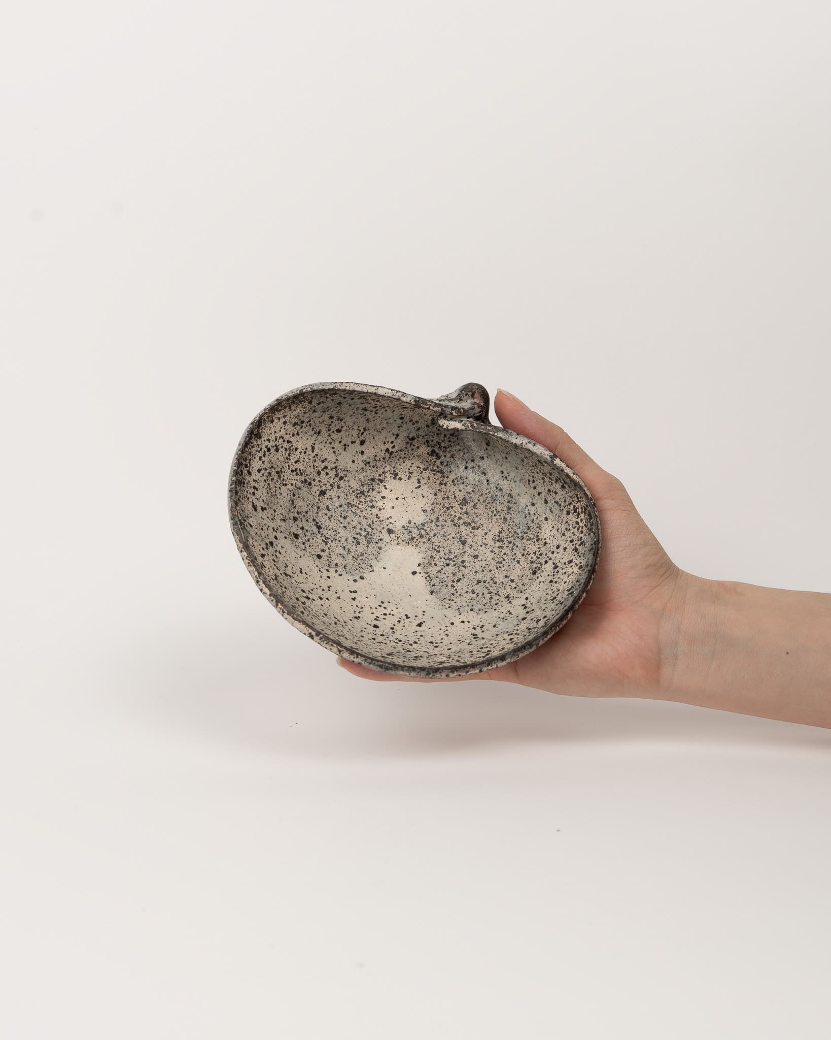 Hand holding a speckled ceramic bowl against a plain background