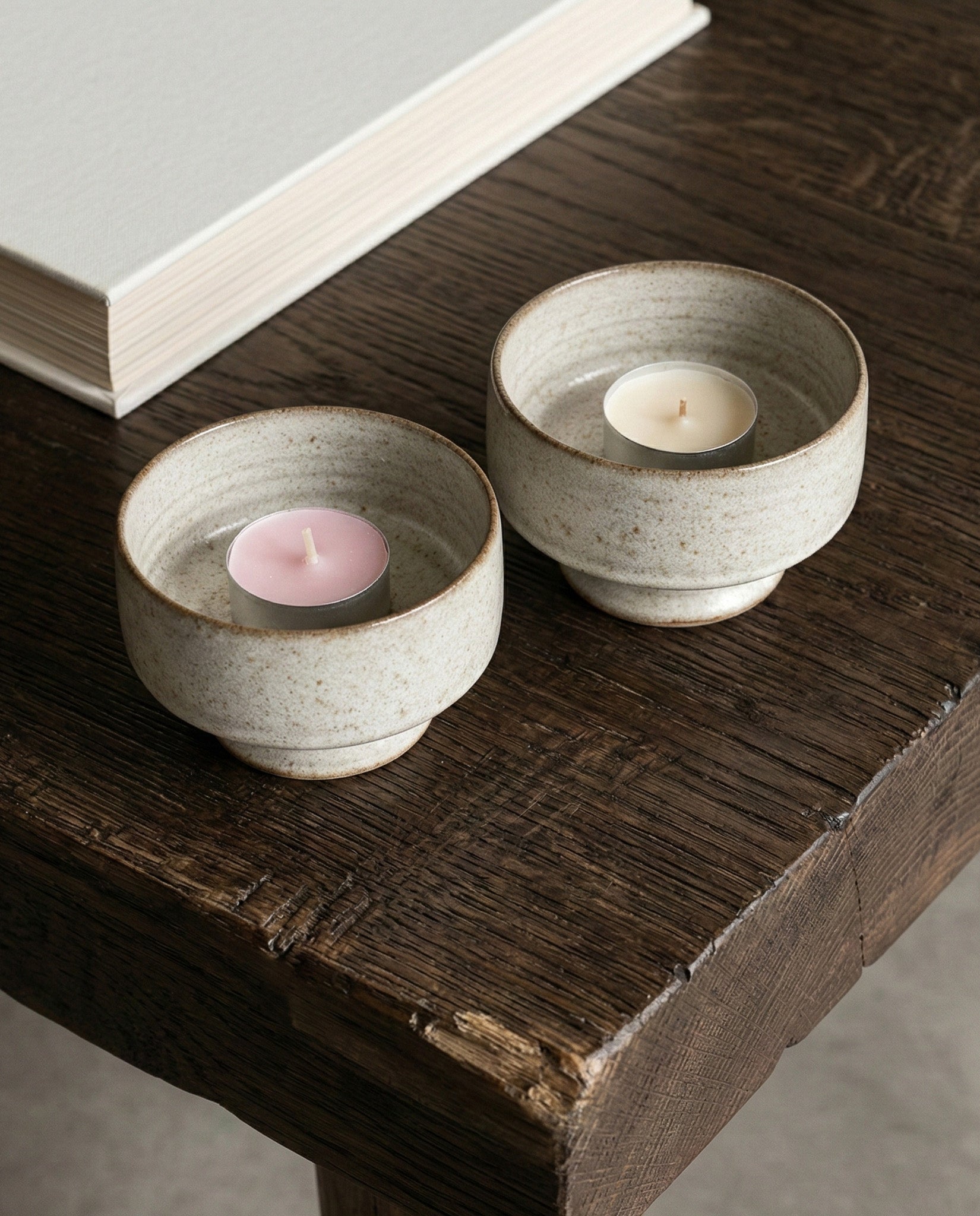 Two ceramic tea light holders with candles on a wooden surface.