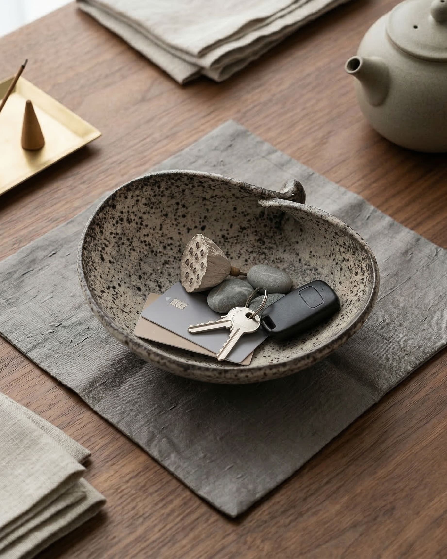 Ceramic bowl with keys and cards on a wooden table with a teapot and napkins.