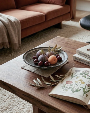 Wooden coffee table with a plate of figs, an open book, and a stack of books in a living room.