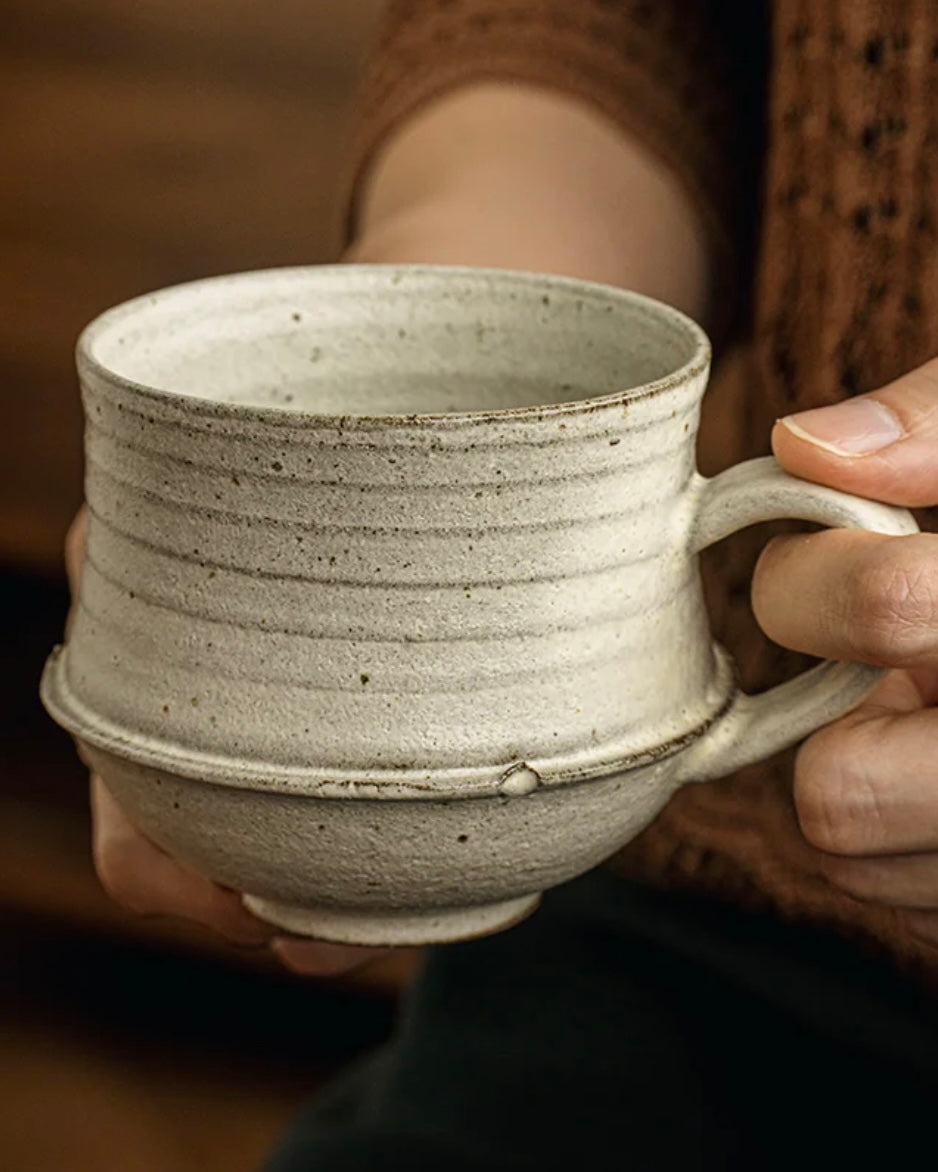 Person holding a rustic ceramic mug with a blurred background
