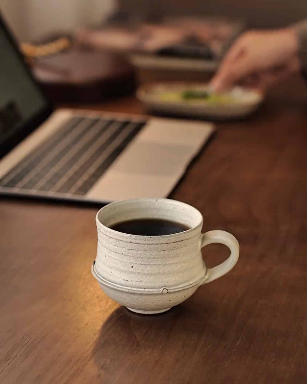 Ceramic mug with coffee on a wooden desk with a laptop and snacks in the background