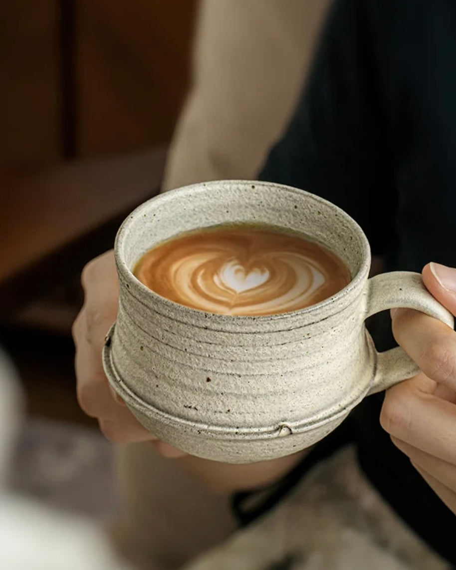 Person holding a textured ceramic mug with a latte art design.
