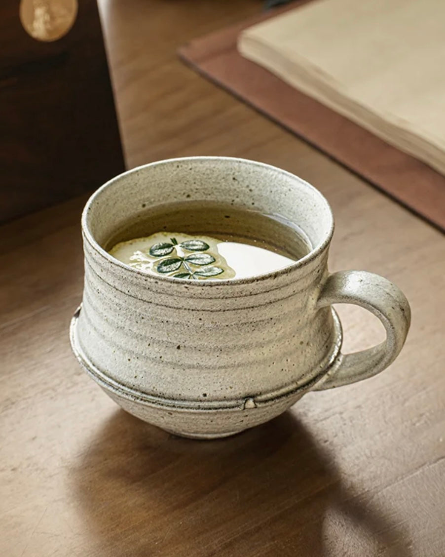 Ceramic mug with a handle on a wooden surface, containing a green liquid.
