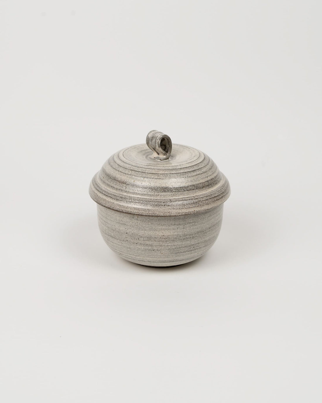 Small ceramic pot with a lid on a kitchen counter next to a towel and spoon