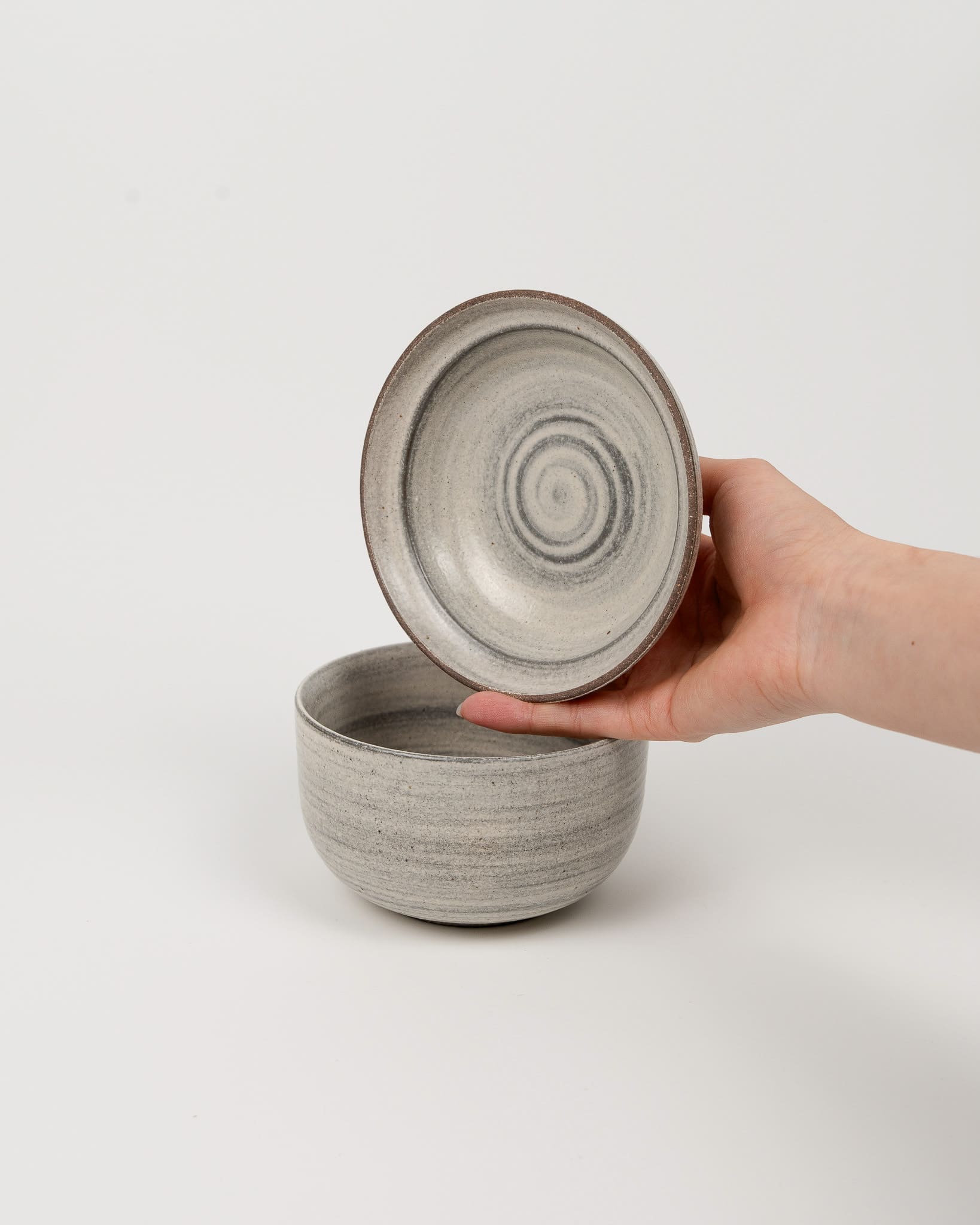 Hand holding a ceramic bowl with lid against a white background