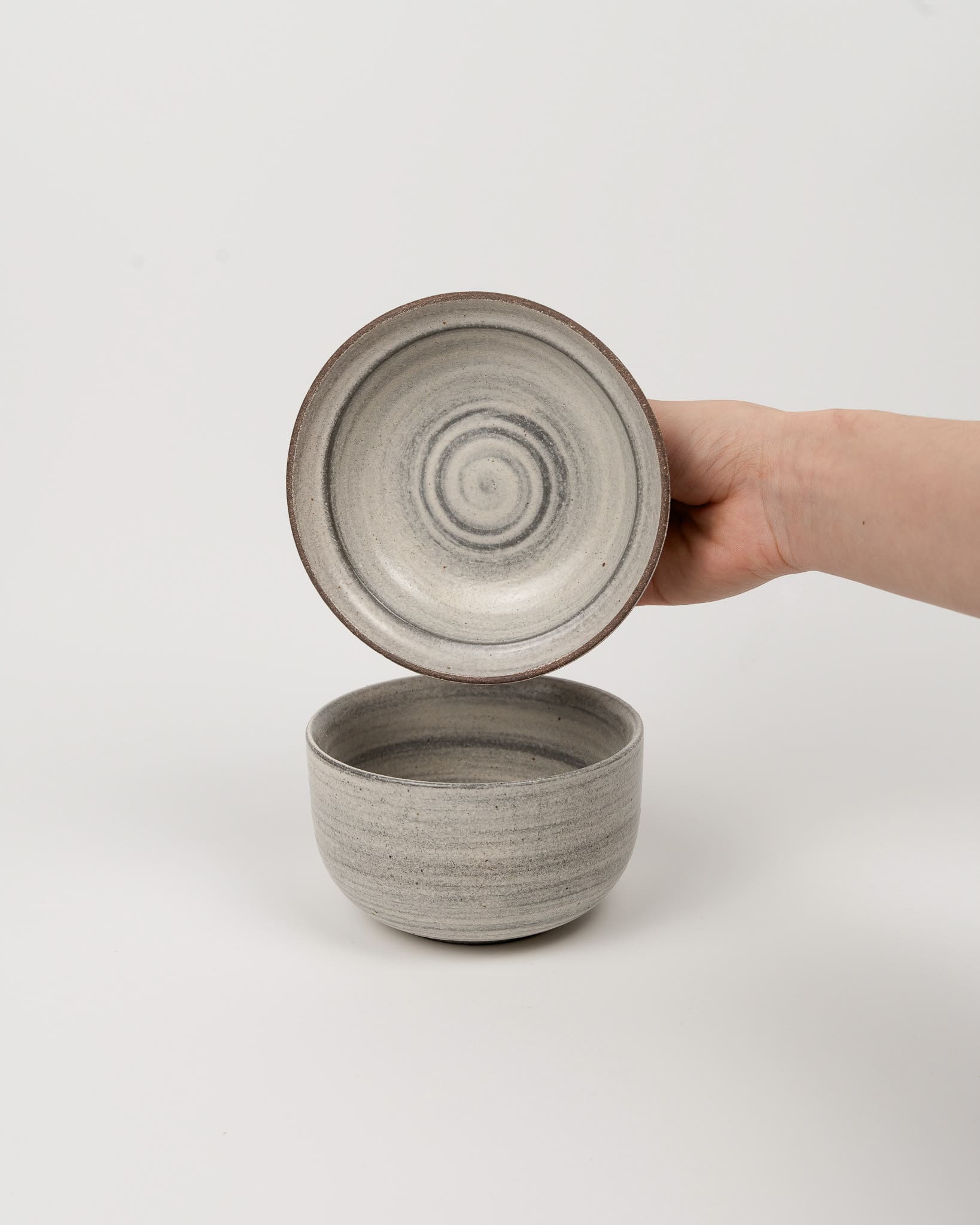 Hand holding a gray ceramic bowl with lid on a white background