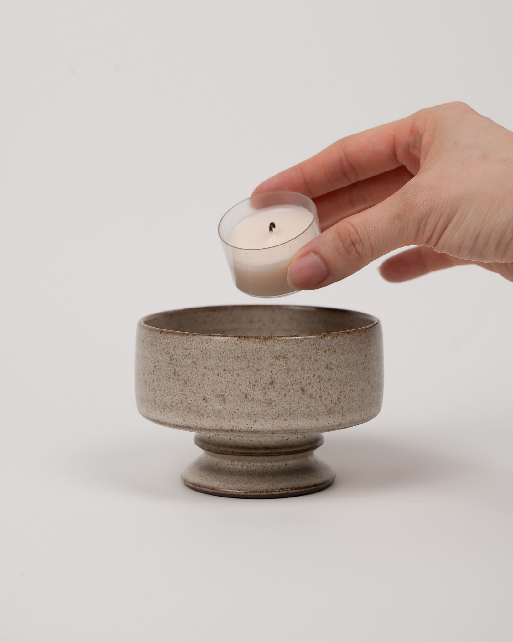 Hand placing a small candle into a ceramic holder on a light background