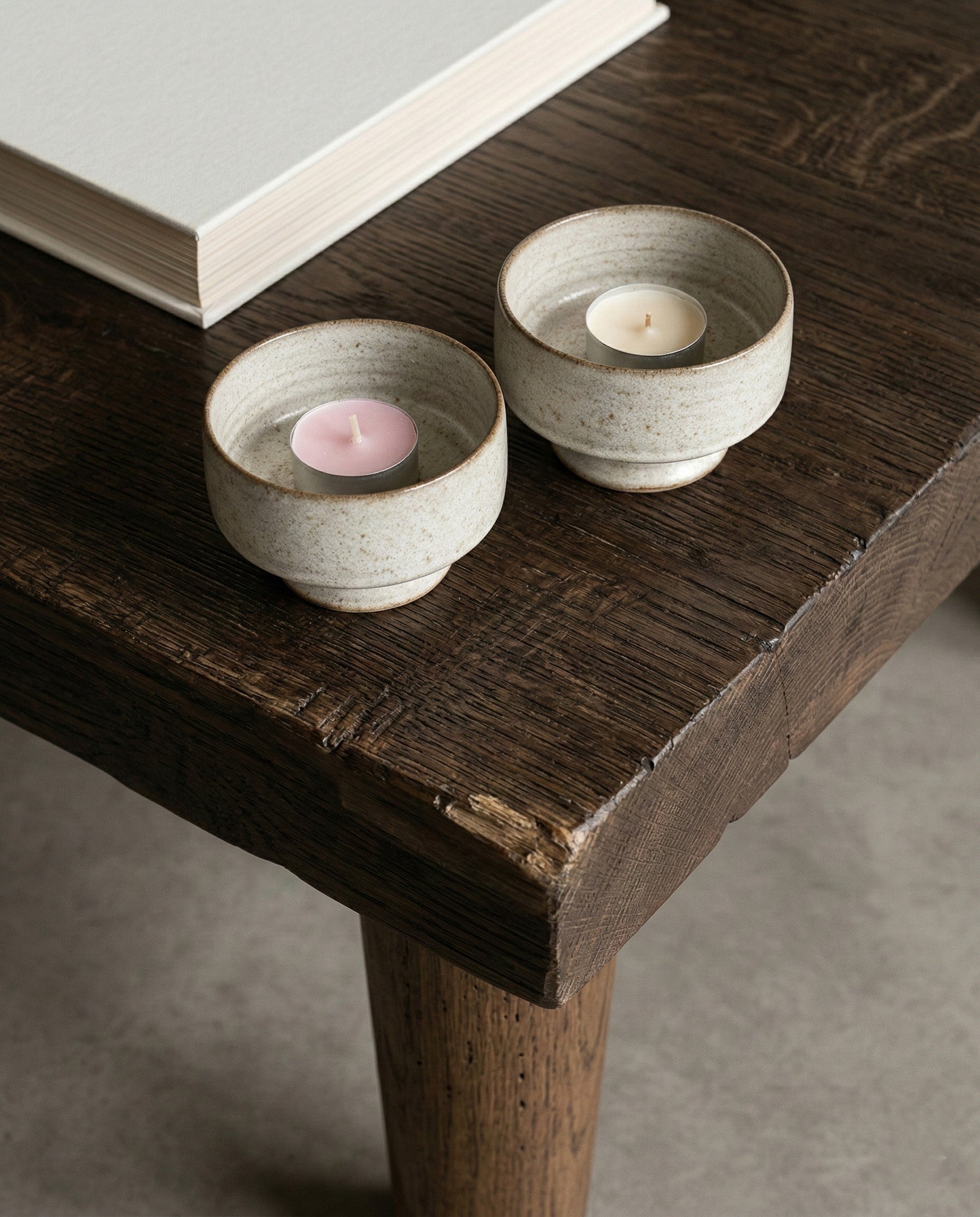 Two ceramic candle holders with candles on a wooden table.