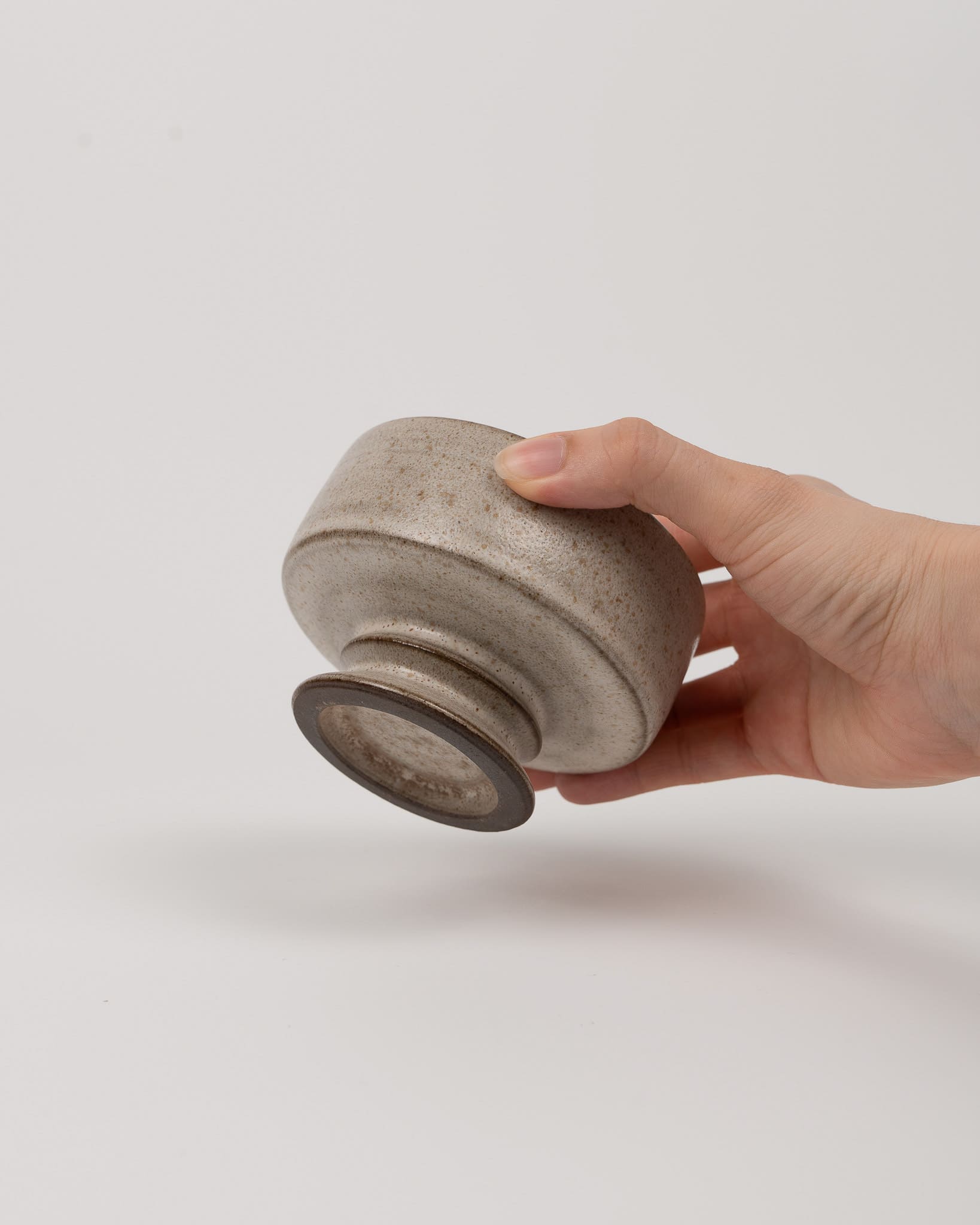 Hand holding a textured ceramic cup against a plain background
