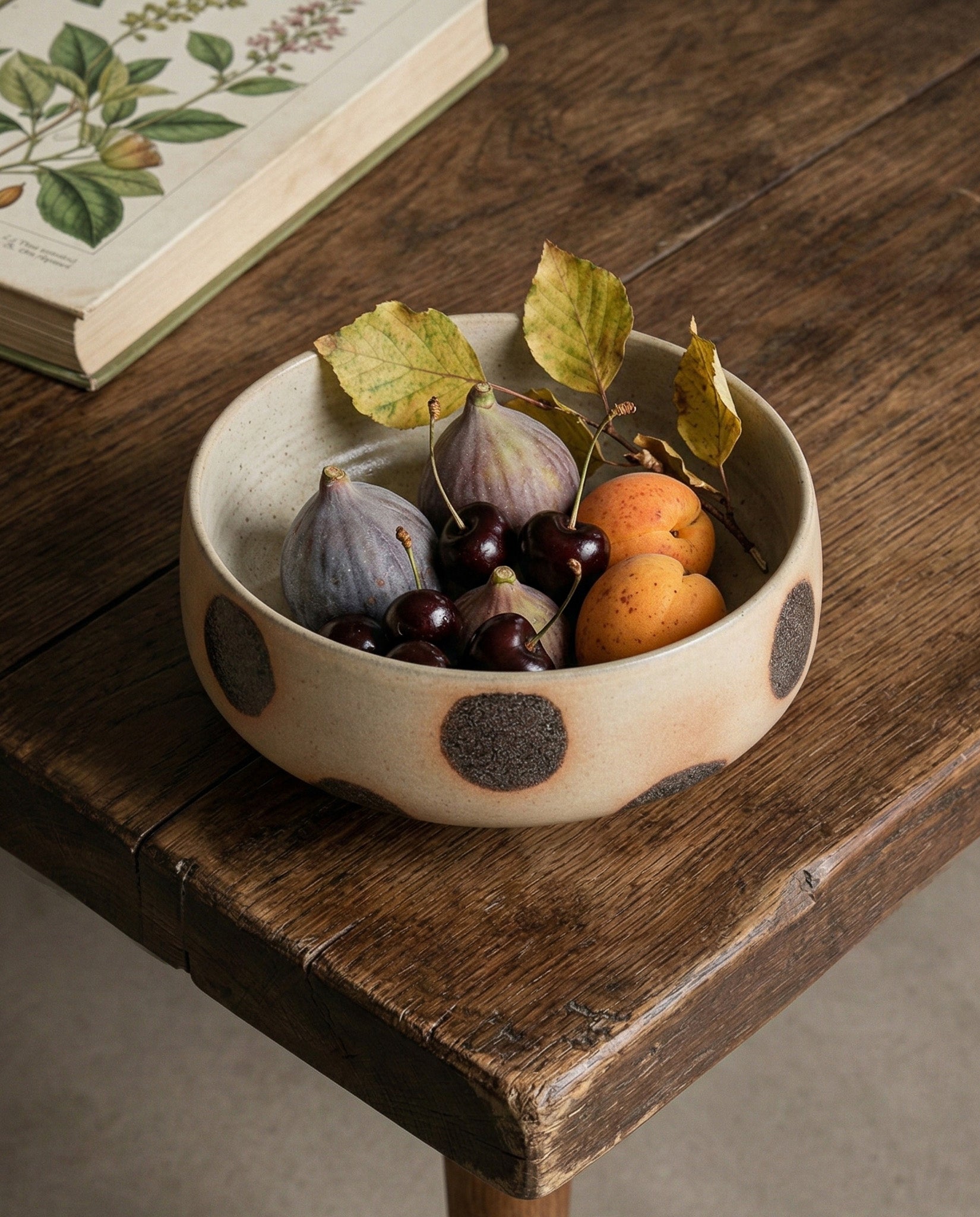 Ceramic bowl with polka dot pattern containing fruits and leaves on a wooden table.