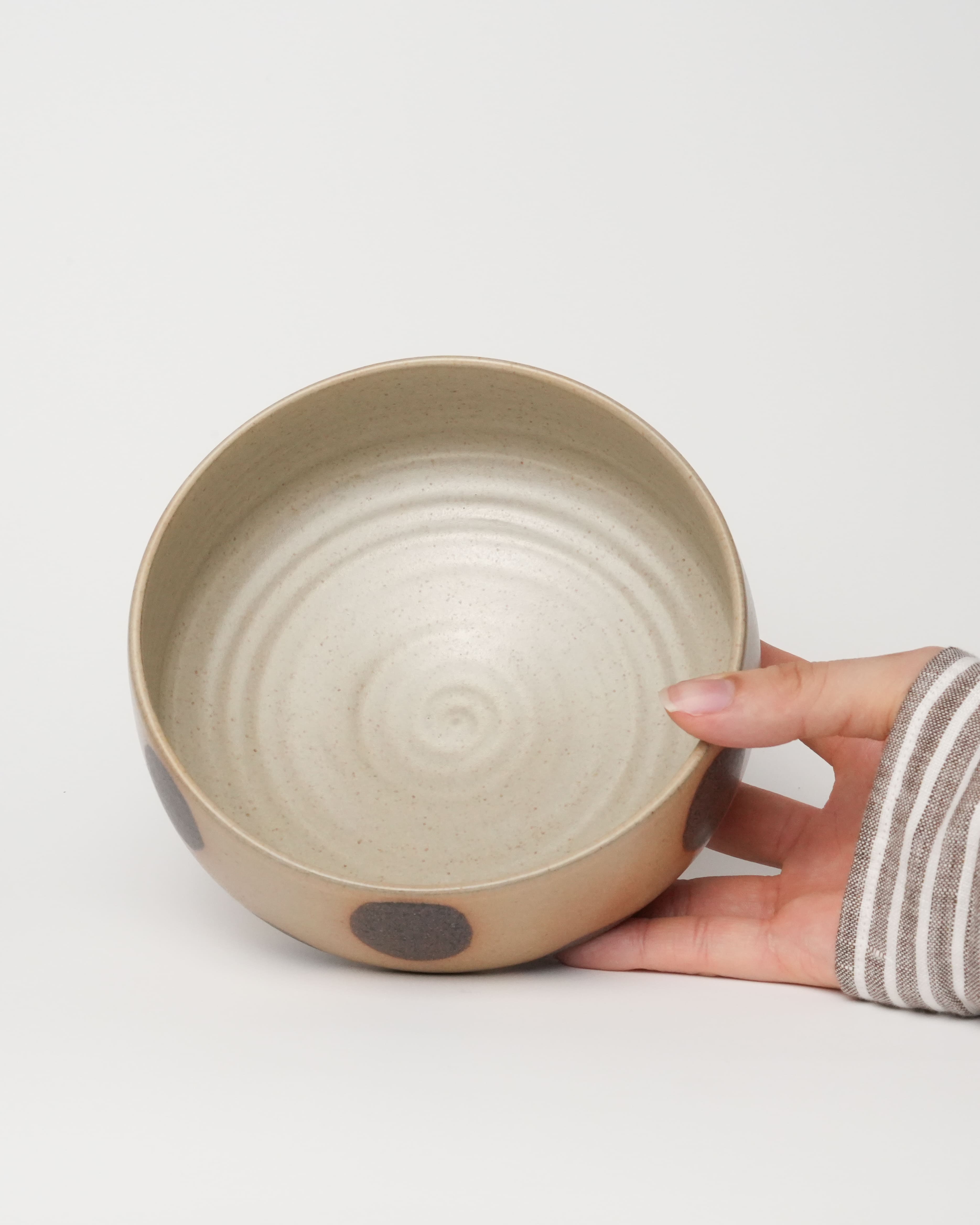 Hand holding a ceramic bowl with a textured surface on a light gray background