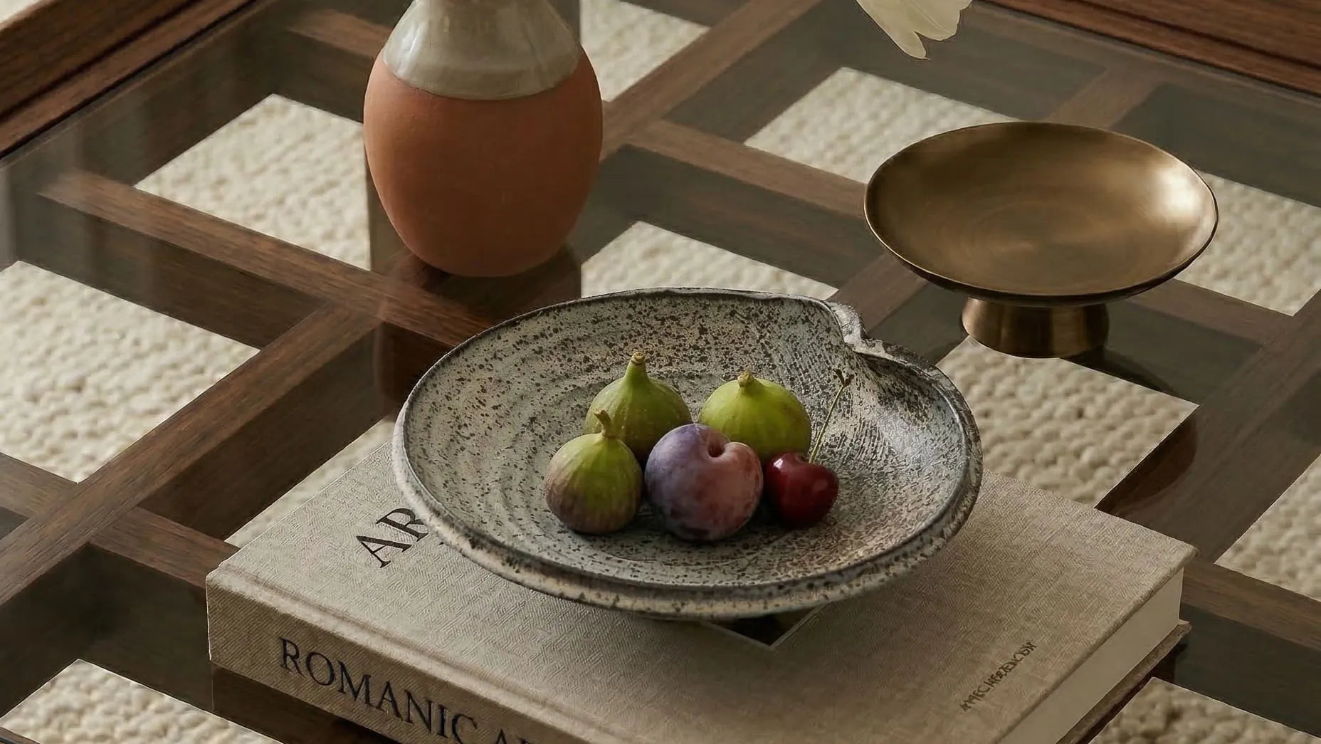 Decorative setting on a coffee table with a bowl of fruit, vase, and books.