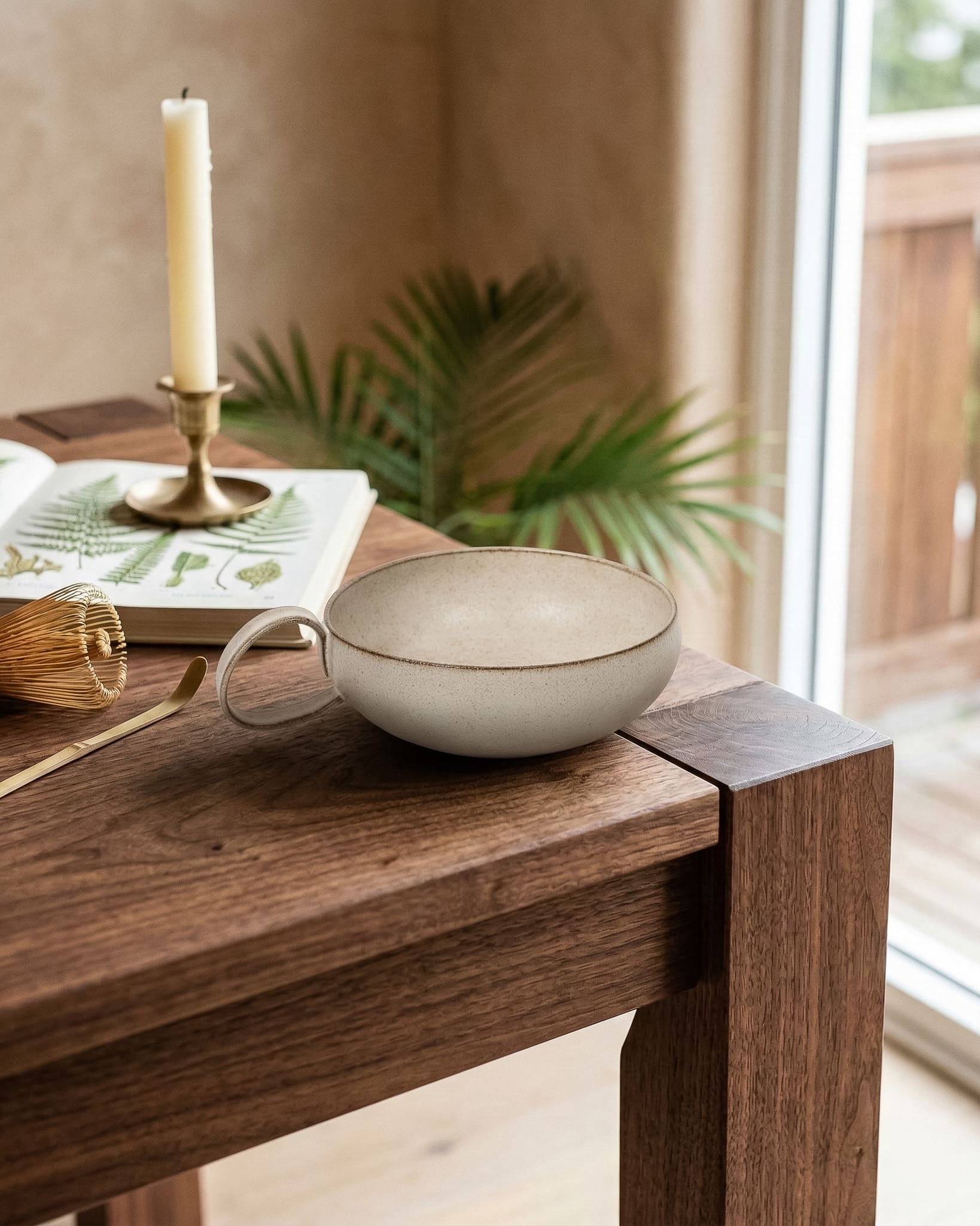 Ceramic bowl on a wooden table with a candle and plant in the background