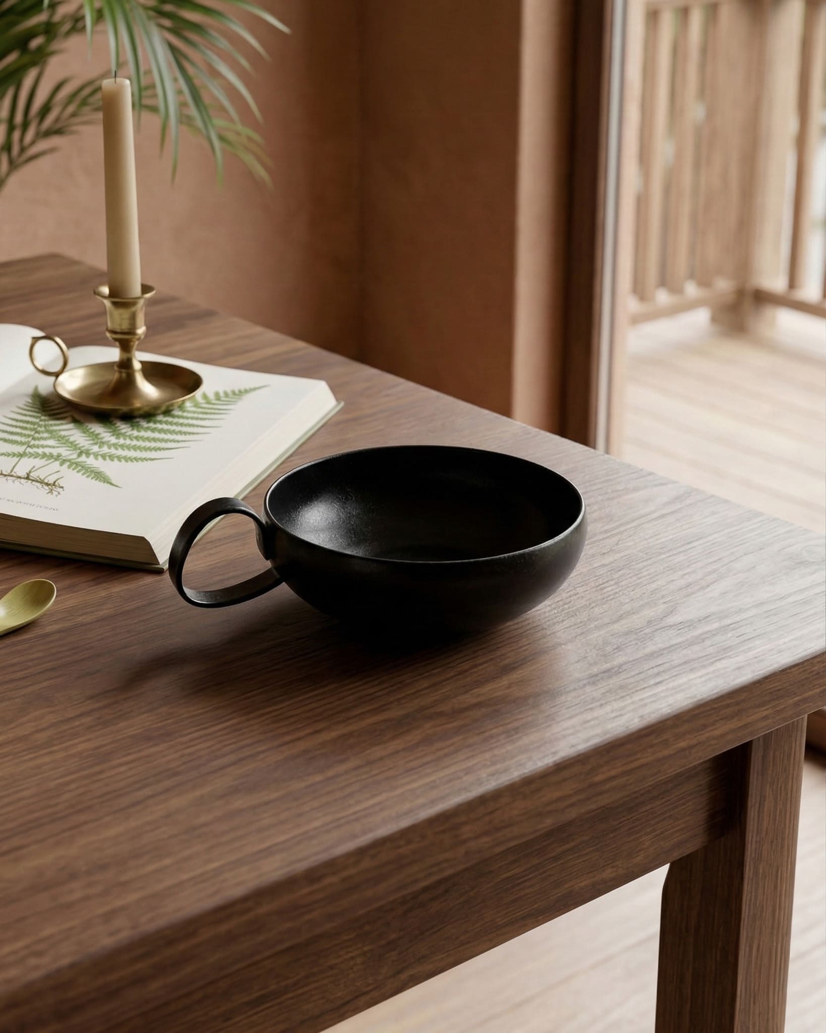Black ceramic cup on a wooden table with a candle and book in the background