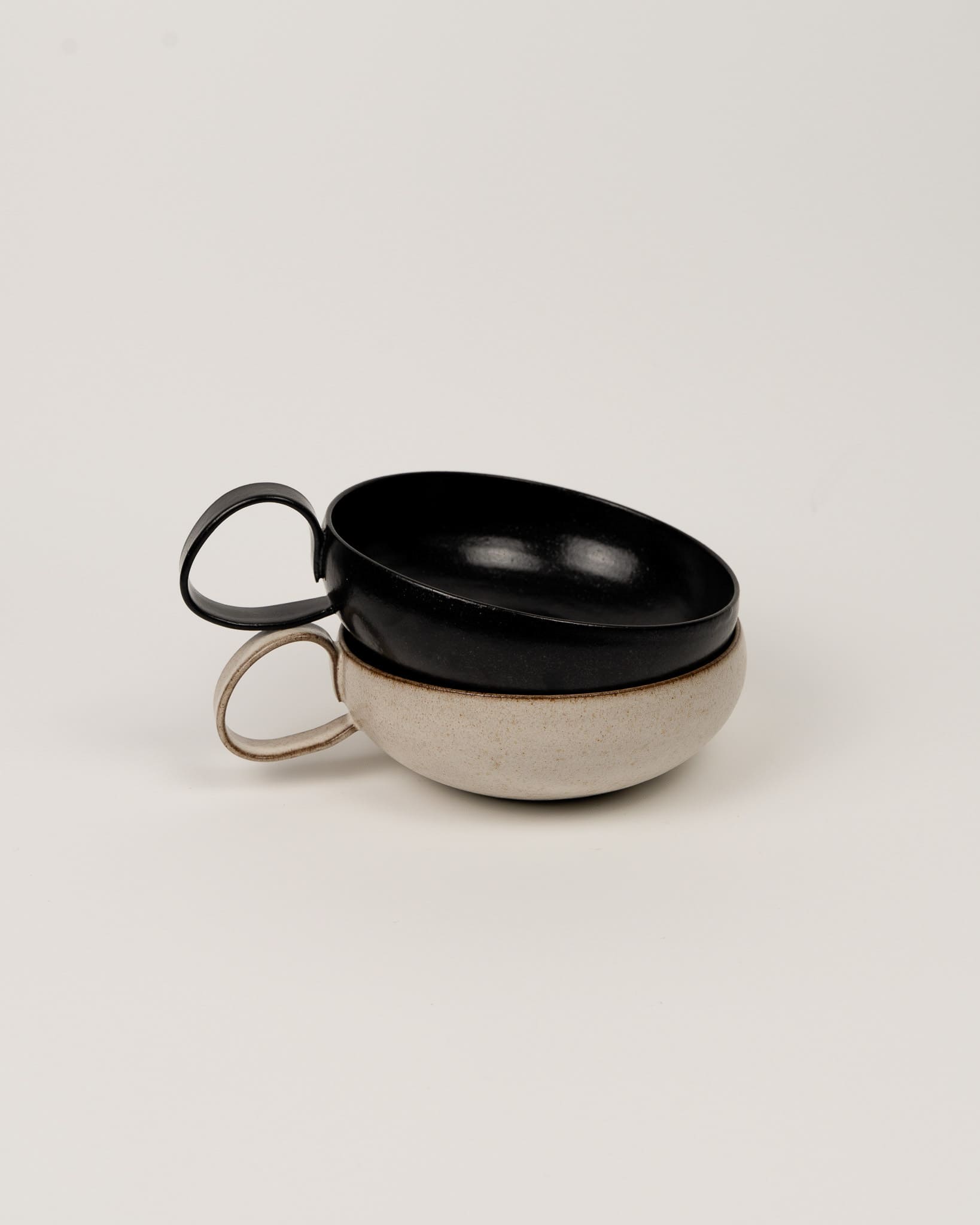 Two ceramic cups, one black and one beige, stacked on a light gray background