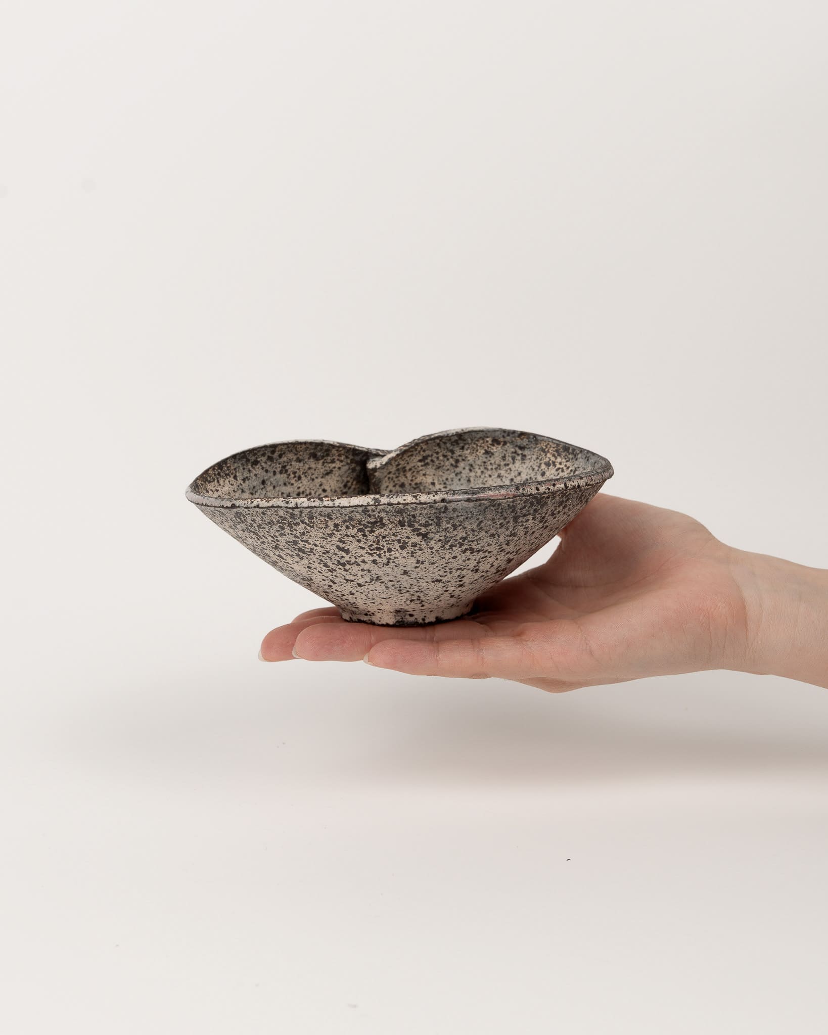 Hand holding a speckled ceramic bowl against a plain background