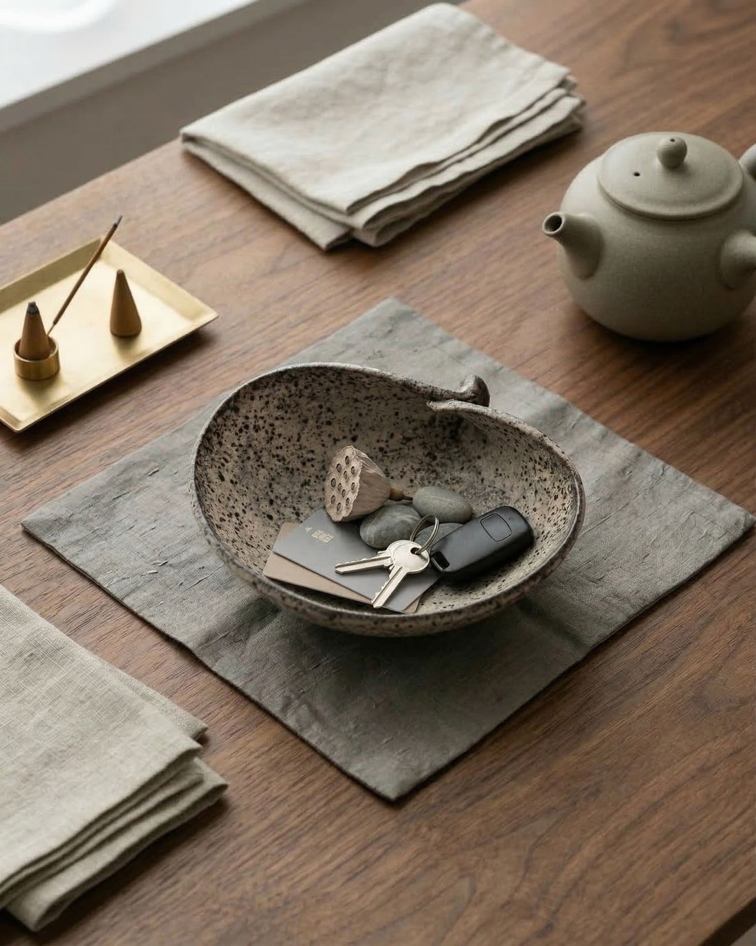 Ceramic bowl with keys on a wooden table with a teapot and napkins.
