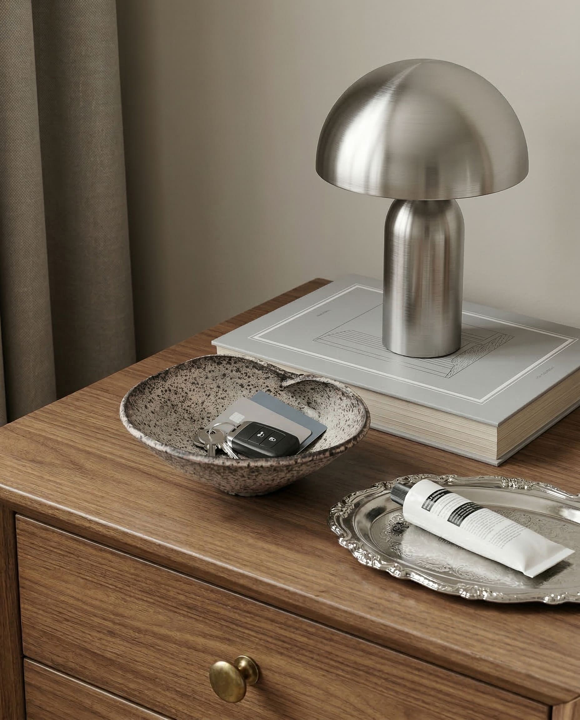 Silver table lamp on a wooden nightstand with a bowl and tray.