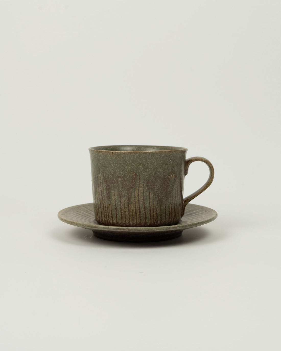 Ceramic cup and saucer on a wooden dresser with a lamp and decorative items.