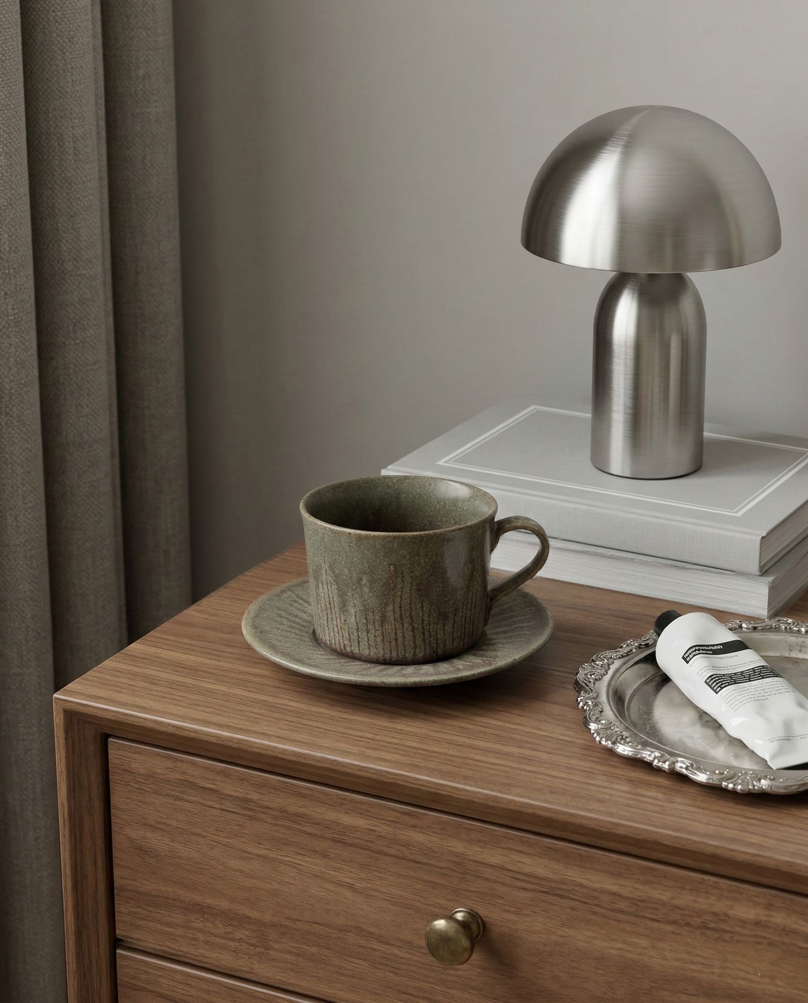 Ceramic cup and saucer on a wooden side table with a metallic lamp and books in the background.