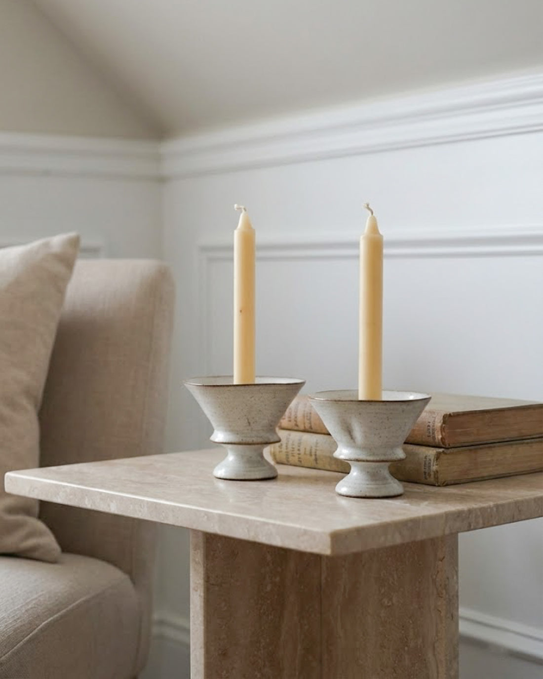 Two beige candles in stone candle holders on a wooden table with a neutral background.
