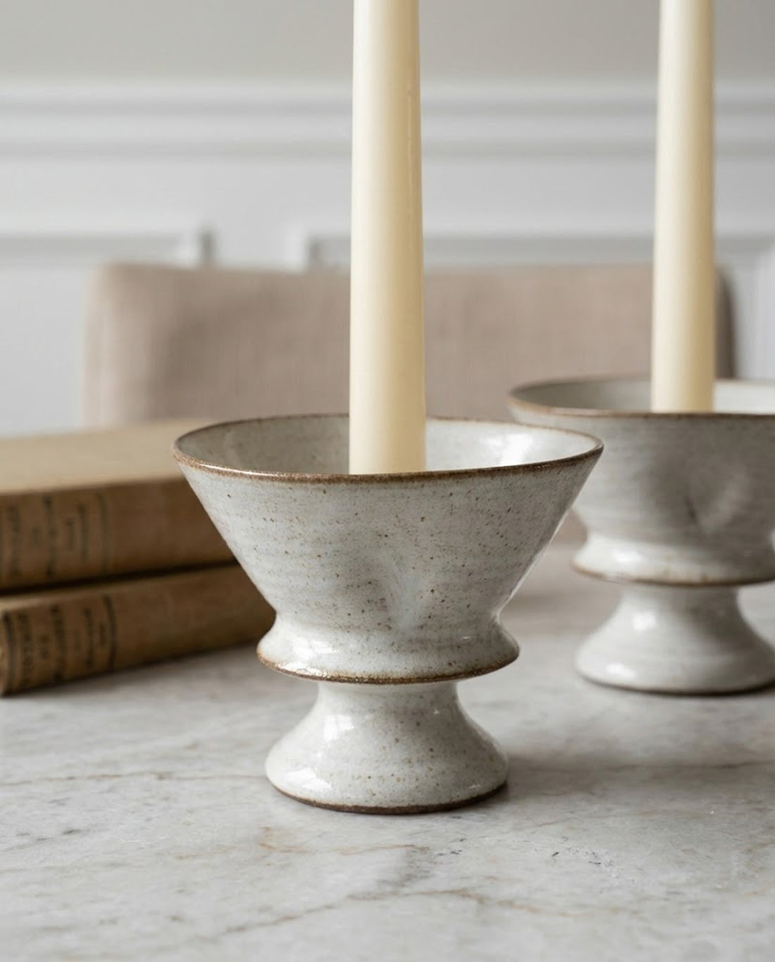 Two beige candles in stone candle holders on a wooden table with a neutral background.