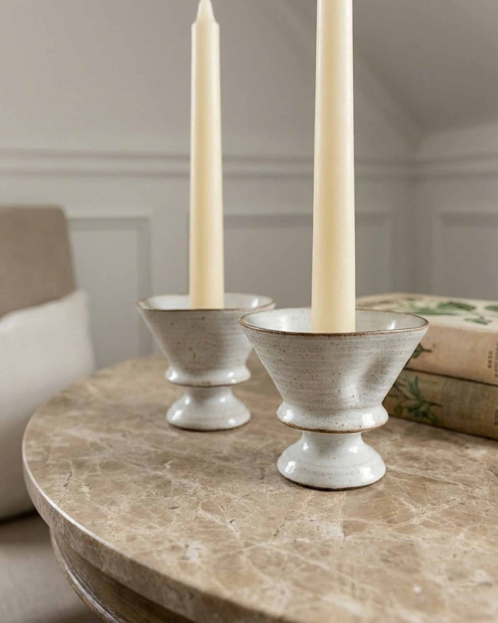 Two white ceramic candle holders with candles on a marble table.